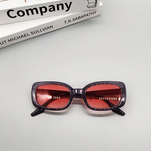 Flat lay of oval sunglasses featuring dark purple frames and transparent red lenses