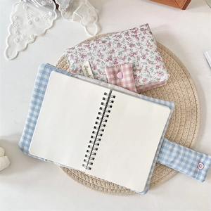 Blue plaid spiral notebook with floral fabric sleeve on a beige woven placemat