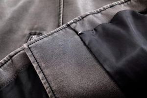Gros plan sur la texture du cuir et les coutures de précision du blouson motard gris