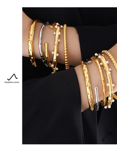 Detail of stacked stainless steel bamboo bracelets with pearls and star patterns on model