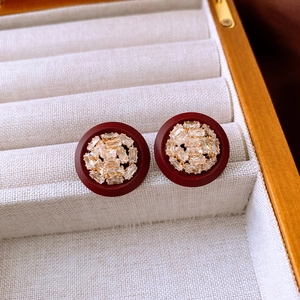 Vue macro de boucles d'oreilles rondes rouge foncé avec cristaux et dorure sur velours beige