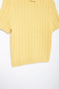 Dettaglio del top in maglia giallo chiaro con trama a trecce e maniche corte