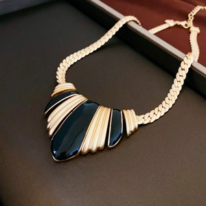 Detail of a vintage gold snake chain necklace with a black enamel fan-shaped pendant