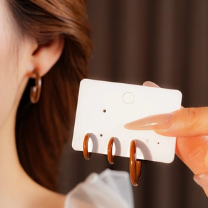 Three pairs of brown acrylic C-shaped hoop earrings in different sizes worn by a model