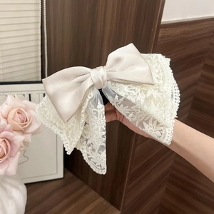 Detail of cream lace bow hair claw clip featuring elegant silk and embroidery texture