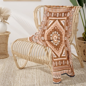 Detail of bohemian flannel blanket with ethnic patterns on a rattan chair in warm setting