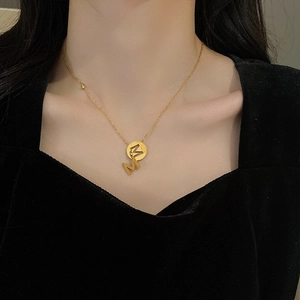 Dettaglio della collana in acciaio al titanio dorato con ciondolo lettera M indossata da modella