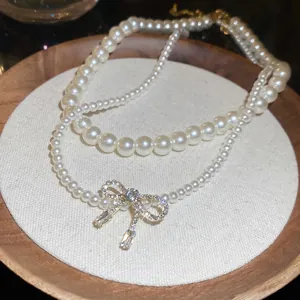 Double-layer pearl necklace featuring a sparkling zircon bow pendant on wooden tray
