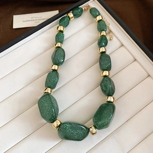 Macro detail of irregular green glitter acrylic beads with golden metal spacers on necklace