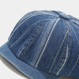 Macro detail of dark blue denim docker cap with vertical striped stitching and top button