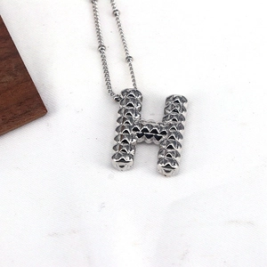 Detailed macro shot of silver H-letter pendant with pyramid stud texture on white fabric