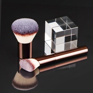 Detail of rose gold makeup brushes with synthetic bristles on reflective surface