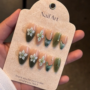 Detail of long almond press-on nails with emerald green marble, gold stars and floral art