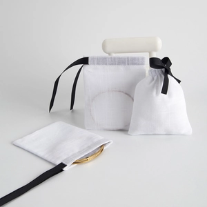 Detail of white cotton jewelry pouch with black satin drawstring and gold bracelet