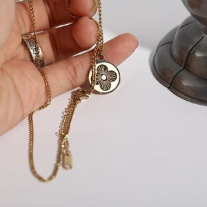 Close-up of golden stainless steel necklace with round white clover pendant detail