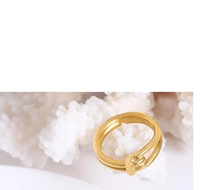 Detailed view of gold plated double band knot ring resting on a white coral texture