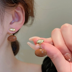 Detailed close-up of brown resin bean stud earrings with golden alloy accents on ears