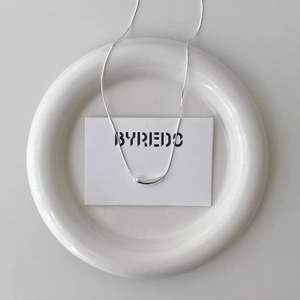 Detail view of a polished 925 sterling silver drop pendant necklace on a ceramic tray