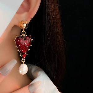 Detail of vintage heart earrings with red enamel and white baroque pearls on a model