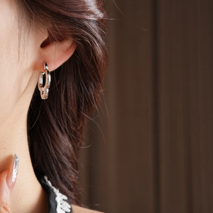 Macro detail of silver clover chain earrings worn by a model on a brown wood background