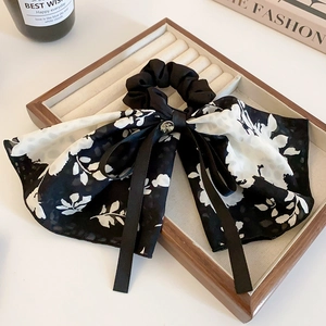 Detail of elegant black and white floral bow hair clip with long ribbon on wood tray