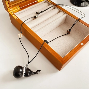Detail of wooden gourd pendant necklace with white beads on a black cord near a wooden box
