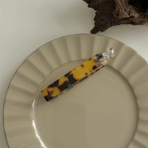 Detail of a large amber tortoiseshell hair claw clip resting on a beige ceramic plate