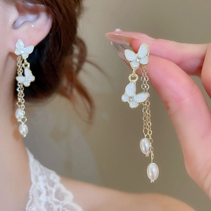 Detail of elegant gold butterfly earrings with long hanging pearl tassels on model