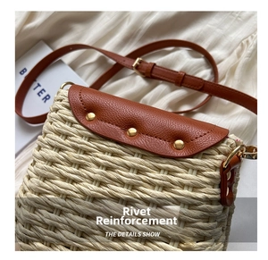 Detail of woven straw crossbody bag featuring brown leather flap and gold stud accents