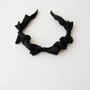 Close-up of black fabric headband with knotted bow design and pleated texture layers