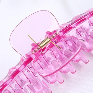 Close-up of the metal spring and tooth detail on a transparent pink plastic hair claw