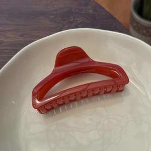 Close-up of translucent orange perfume bottle hair claw clip on ceramic dish