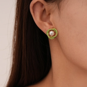Detailed close-up of a vintage pearl earring with green rhinestones on a model's ear