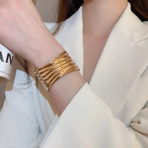 Close-up of golden wide cuff bracelet with wavy metallic texture on a white suit sleeve