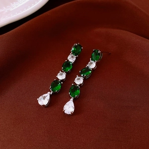 Close-up of silver drop earrings with green and clear crystals on dark velvet
