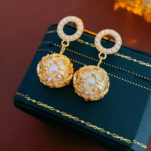 Detailed view of luxury gold cage pearl earrings with rhinestones on a green jewelry box