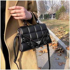 Detail of black quilted leather handbag featuring a triangle metal buckle and chain strap