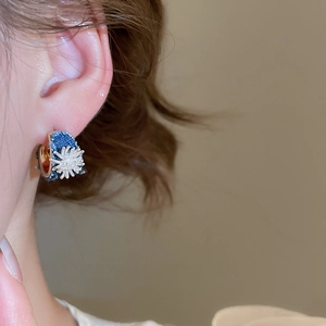 Detail of blue denim C-shaped hoop earrings with silver snowflake and diamond accents