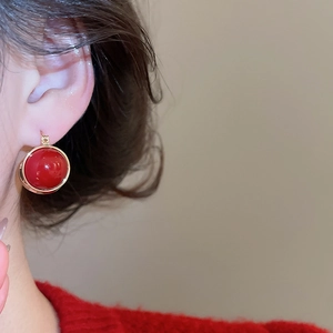 Close-up of elegant red zircon stud earrings with gold rim worn by a model