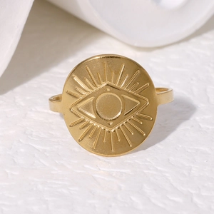 Gold stainless steel evil eye ring with sunburst engraving on a white textured surface