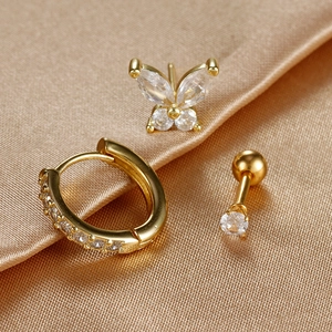 Golden three-piece earring set with butterfly stud and zircon hoops on satin background