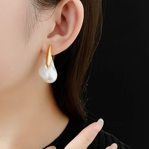 Close-up of gold-plated earrings with irregular white pearls on model with black background