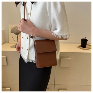 Sac bandoulière marron en similicuir porté par un mannequin dans un décor minimaliste
