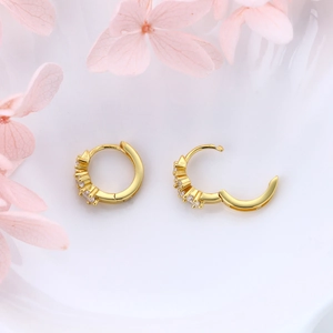 Detail view of gold hoop earrings with white zircon stones on white background and petals