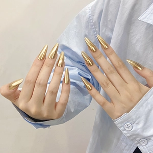 Glossy champagne gold mirror finish stiletto nails on hand with a minimalist backdrop