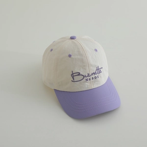 Detail of color-block kids baseball cap featuring purple embroidery on cream fabric