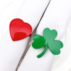 Close-up of red heart and green clover metal napkin rings on white cloth napkins