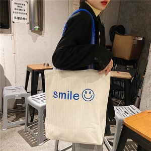 Detail of off-white canvas tote bag with blue smile embroidery and wavy woven strap