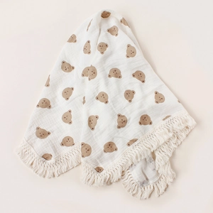 Detail of white cotton baby blanket with brown bear prints and decorative tassel trim