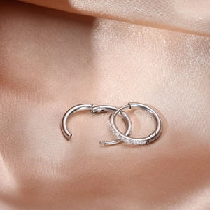 Close-up of polished silver hoop earrings with inset crystals on champagne silk fabric